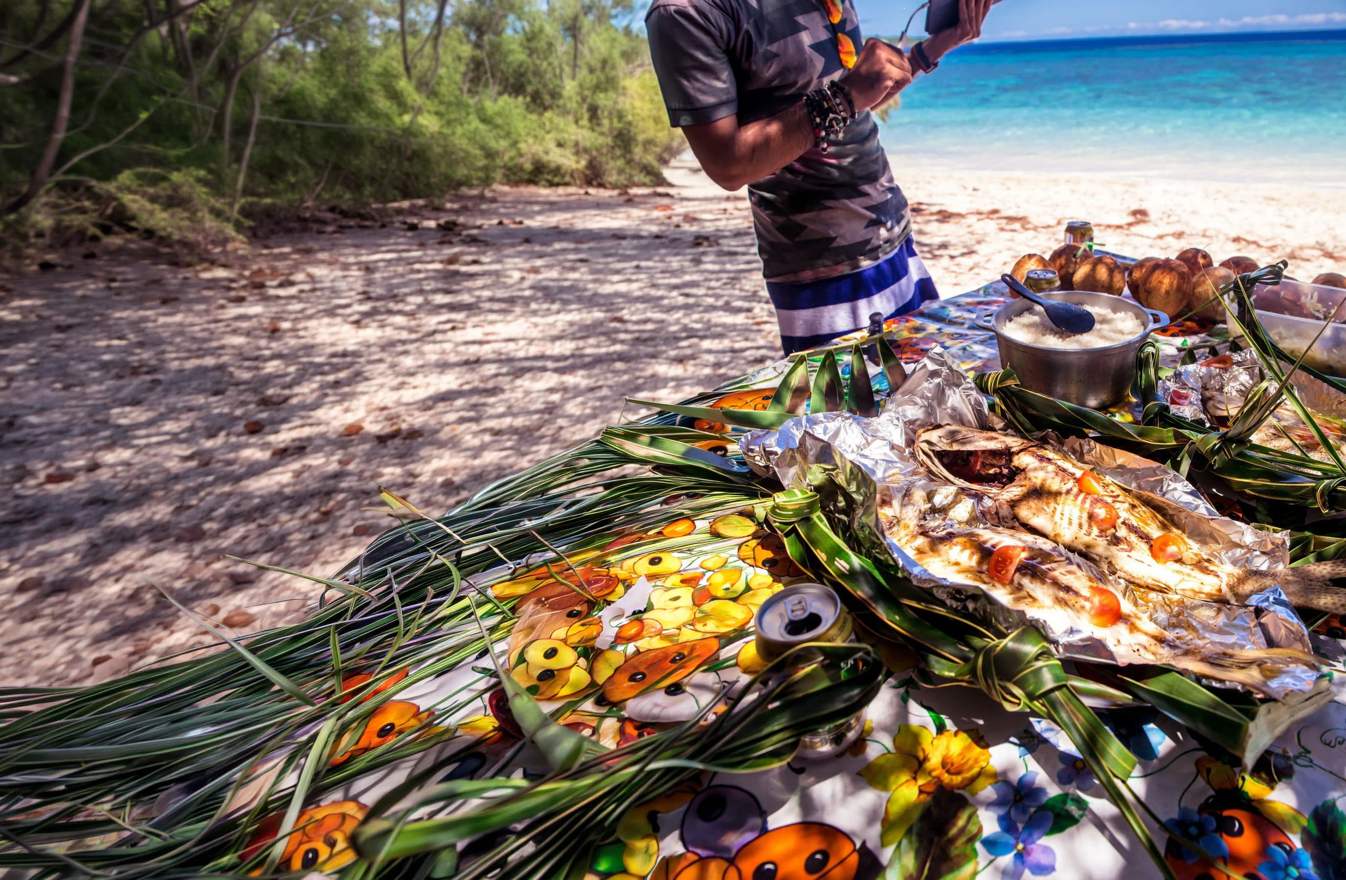 Grilled fish and rice on a floral tablecloth at a tropical beach with turquoise water.